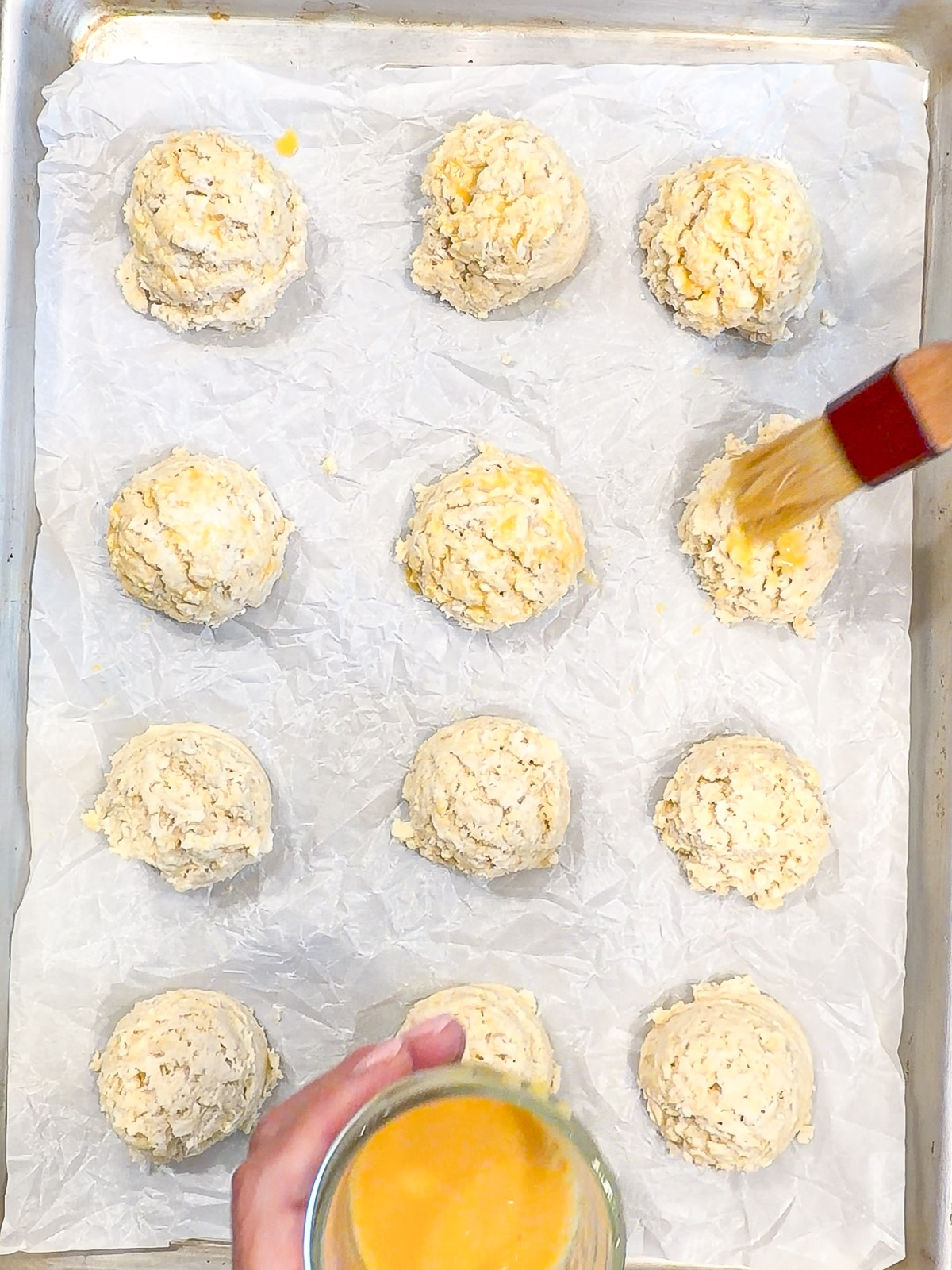 Brushing an egg wash on top of unbaked drop biscuits.