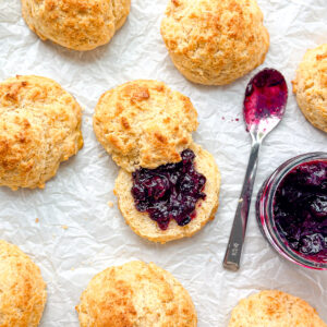 Cornbread biscuits and a pot of jam with a spoon on parchment paper.