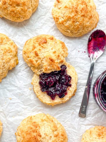 Cornbread biscuits and a pot of jam with a spoon on parchment paper.