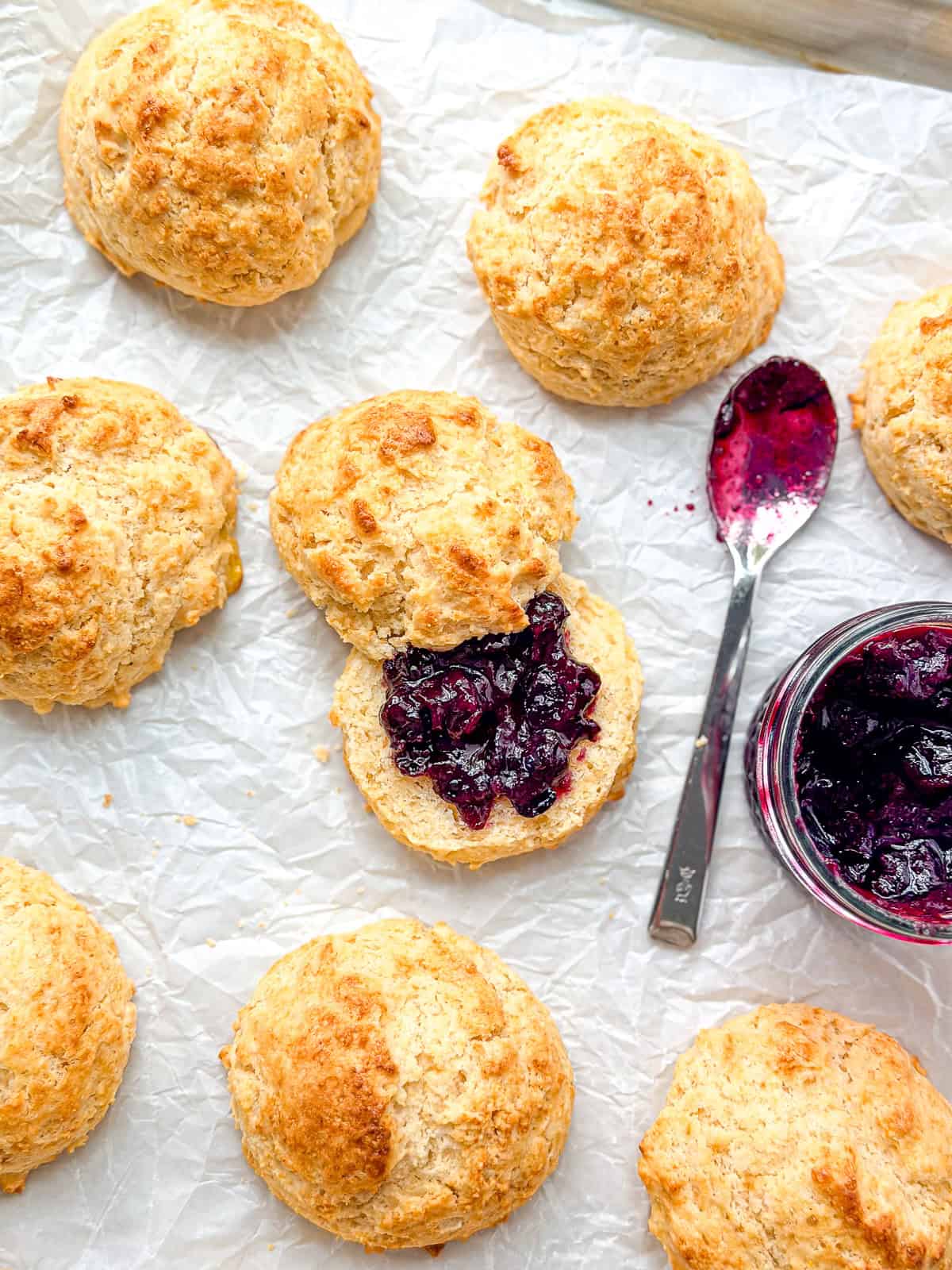Cornbread biscuits and a pot of jam with a spoon on parchment paper.