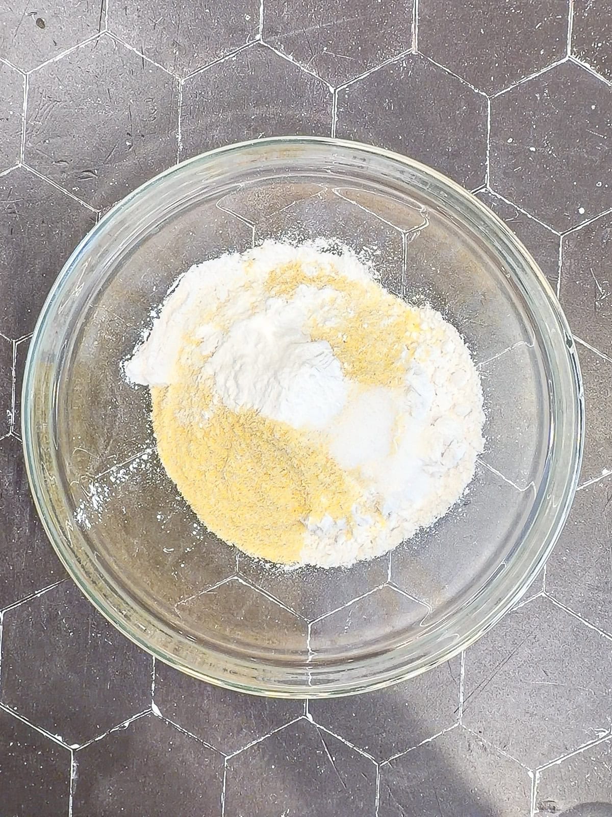 Dry ingredients for cornbread biscuits in a glass bowl.