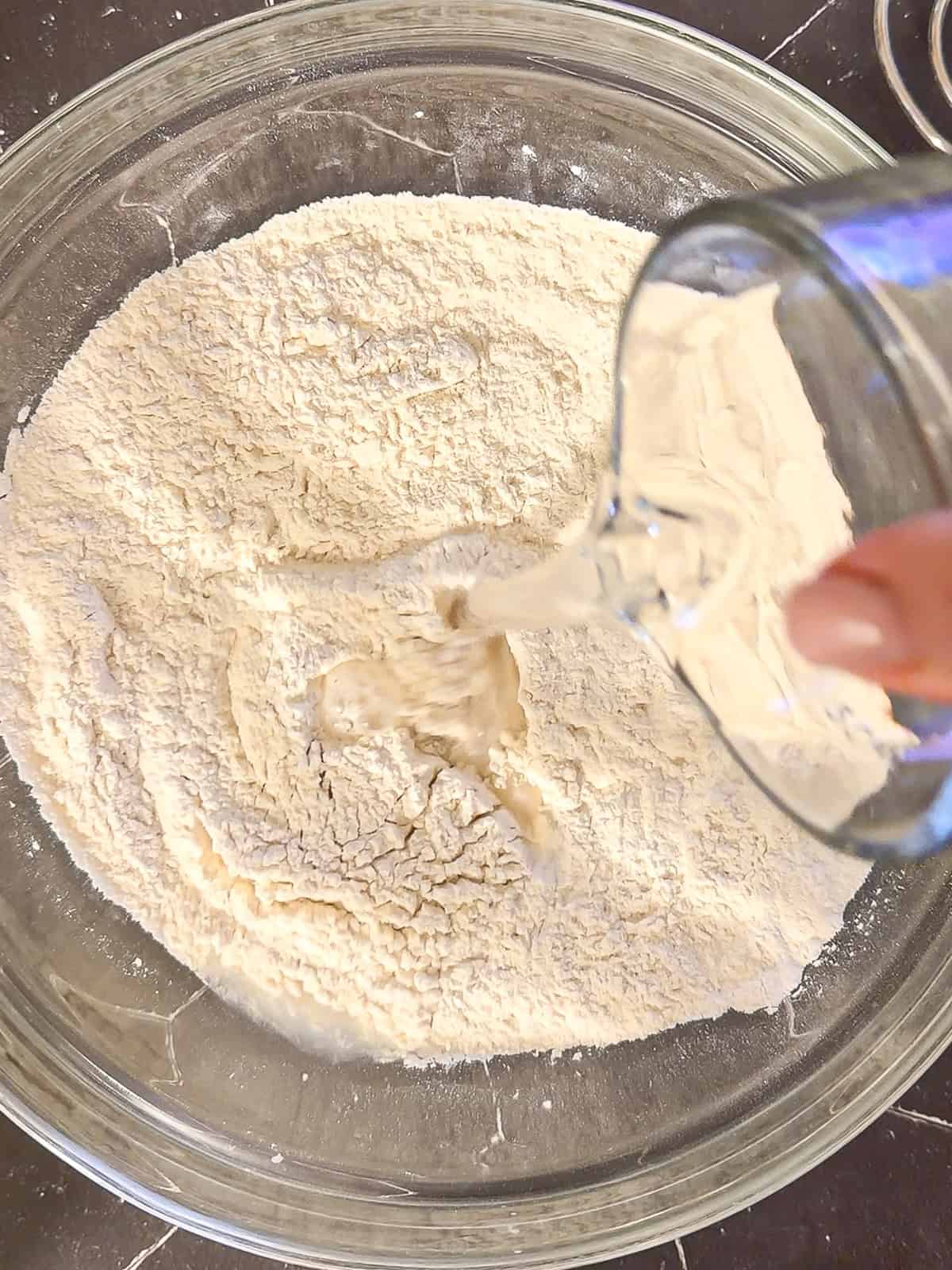 Adding water to dry ingredients to make bread dough.