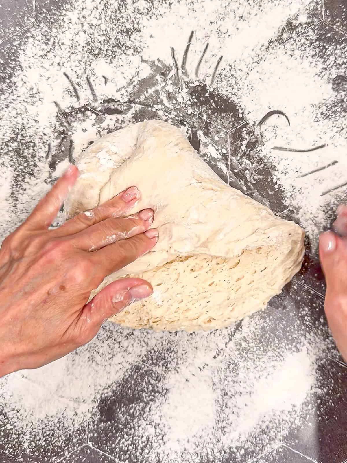 Folding a very sticky dough into a ball shape on a well-floured counter.