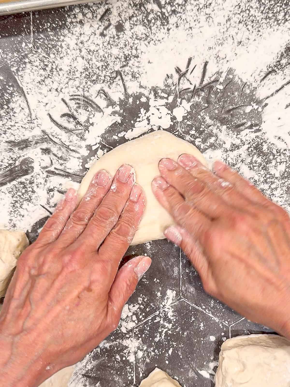 Flattening a piece of dough on a floured counter.