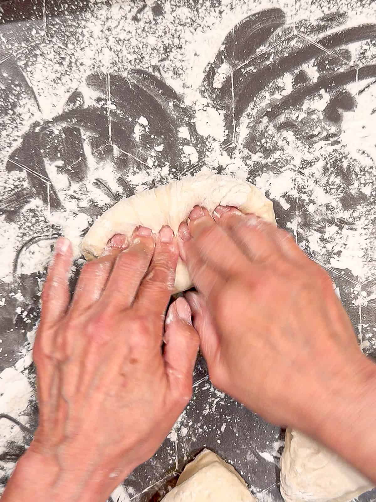 Folding a piece of dough into a oblong roll shape.