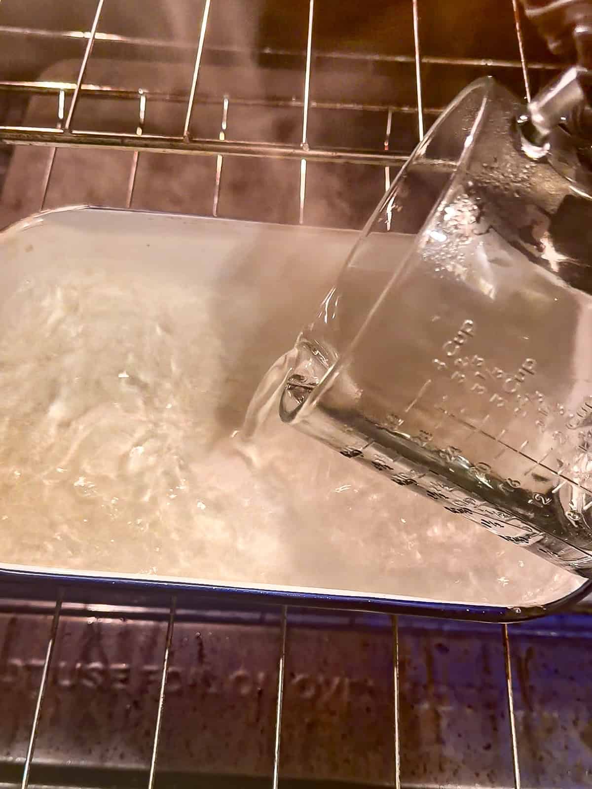 Pouring water into a metal pan on a rack in the oven.