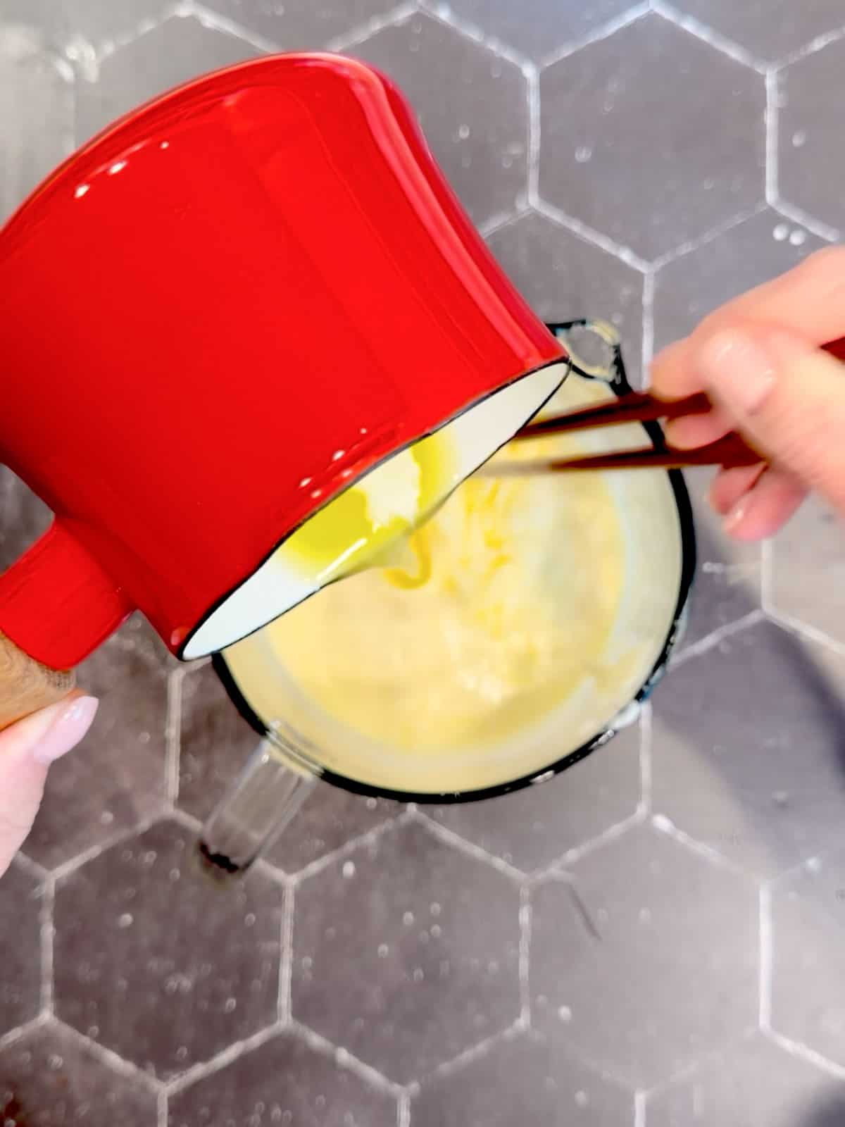 Pouring melted butter into wet ingredients for pancakes.