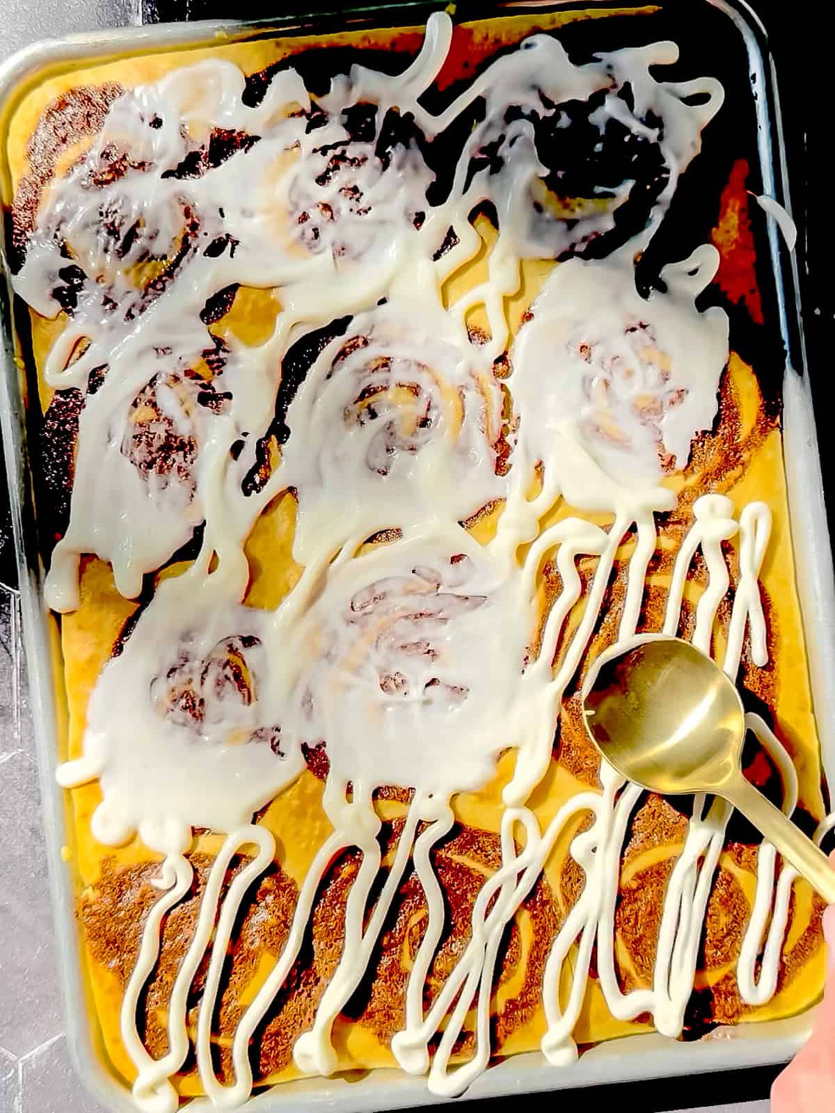 Spreading icing on top of baked cinnamon roll sheet pan pancakes