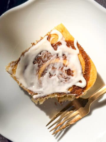 An iced slice of cinnamon roll pancake on a white plate.