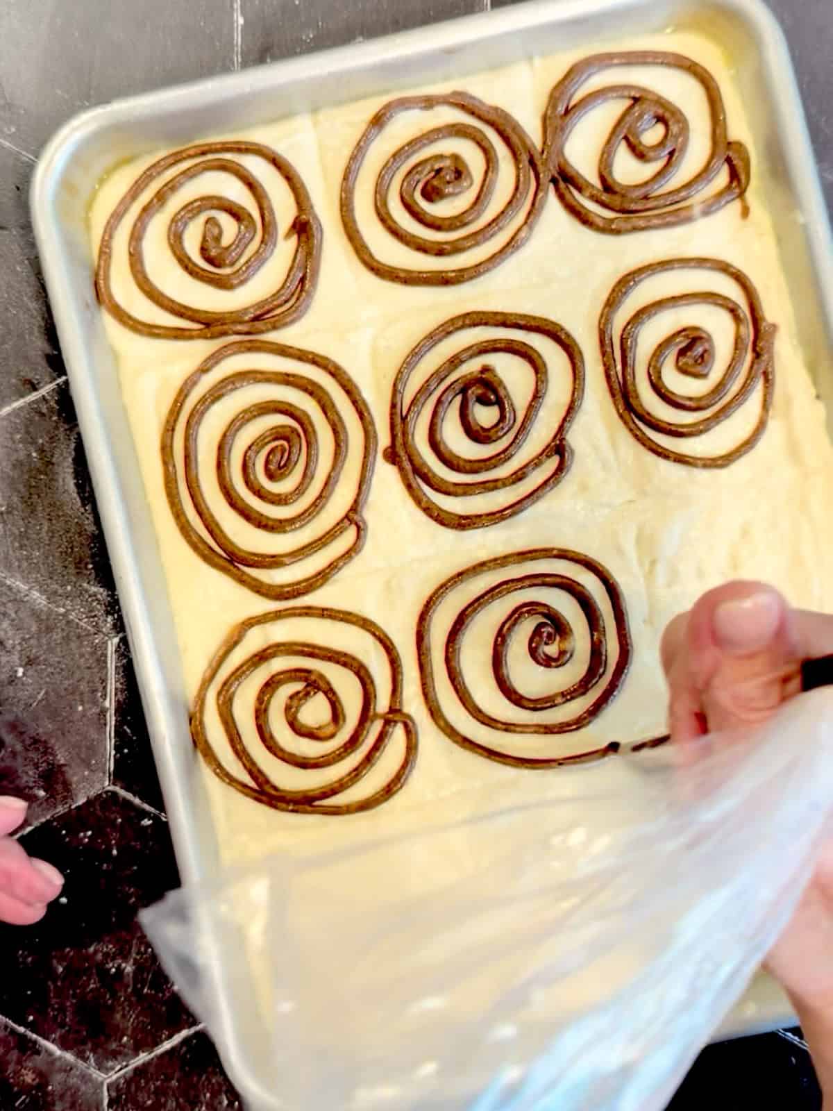 Piping swirls of cinnamon filling on top of pancake batter in a sheet pan.