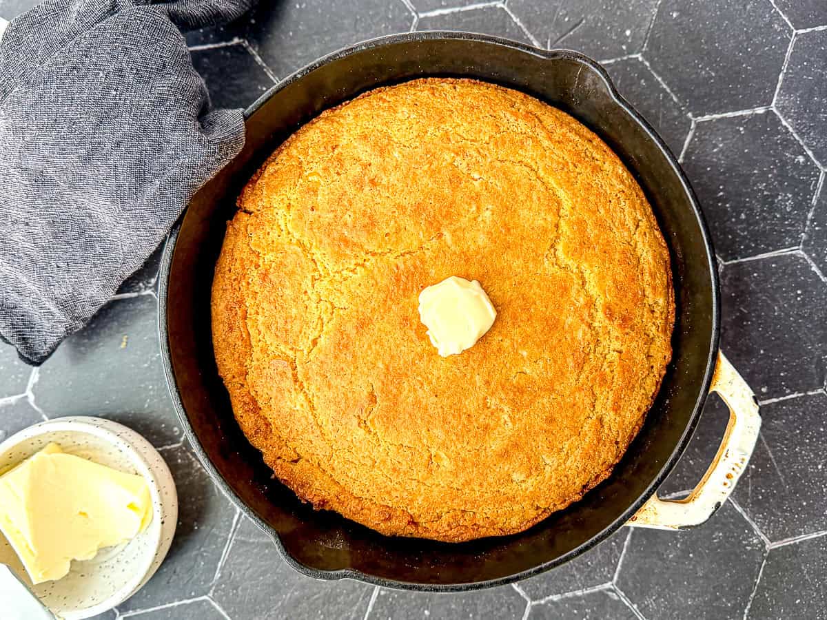 A cast-iron pan of cornbread with a pat of butter on it.