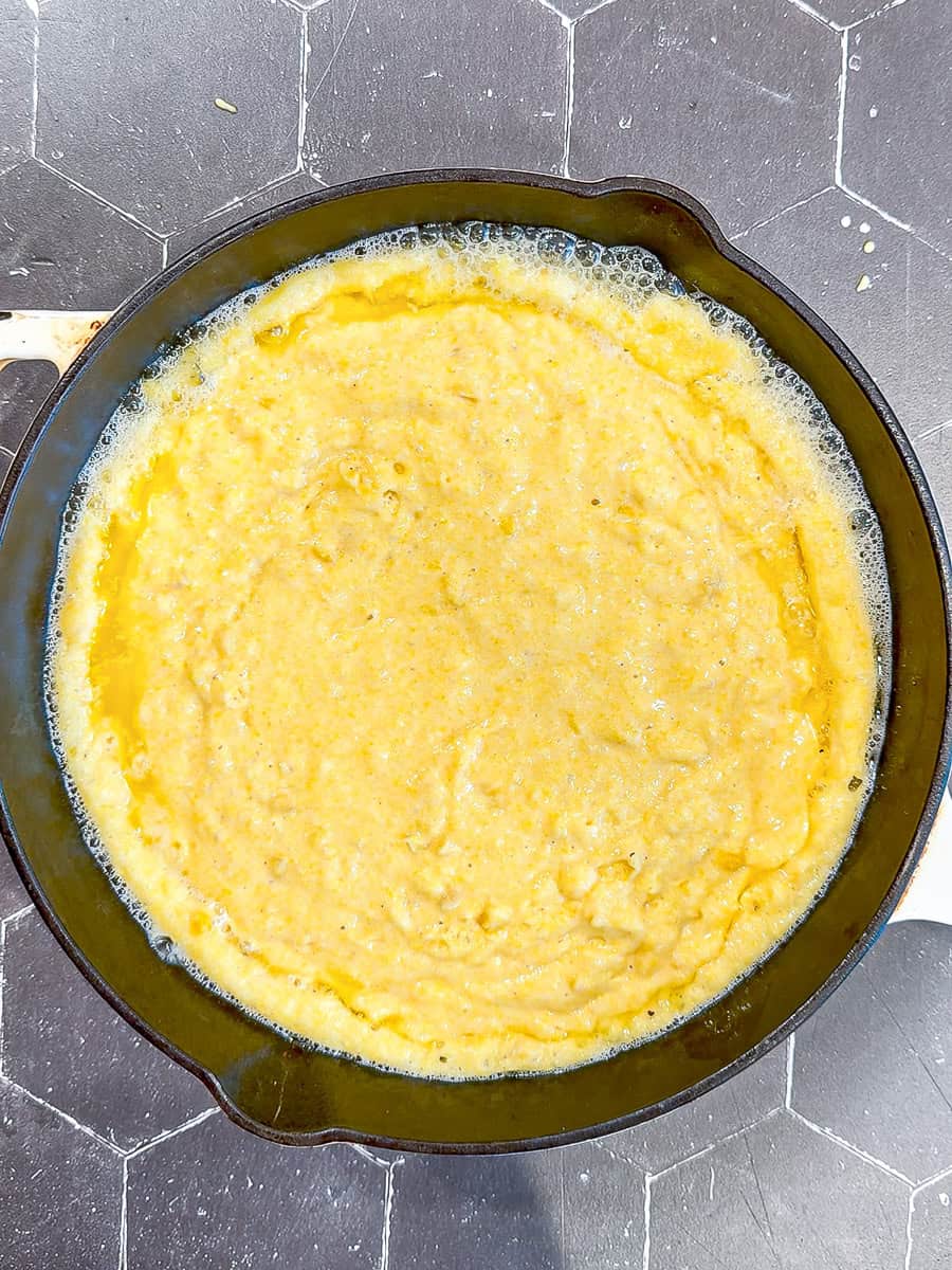Cornbread batter poured into a sizzling hot buttered cast-iron pan.