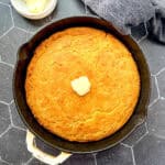 A cast-iron pan of cornbread with a pat of butter on it.