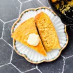 Two slice of cornbread on a scalloped plate next to a pan of cornbread.