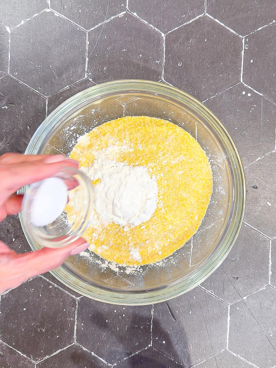 Combining dry ingredients in a glass bowl for cornbread.
