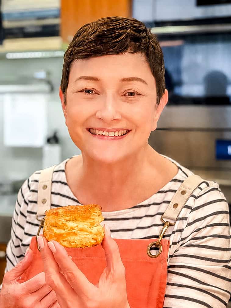 An image of Cynthia holding a biscuit in front of ovens.