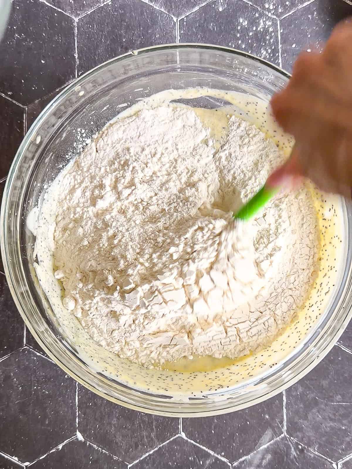 Mixing dry ingredients into wet ingredients to make muffins in a glass bowl.
