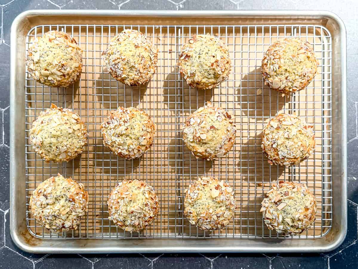 A dozen almond poppy seed muffins cooling on a wire rack set in a sheet pan.