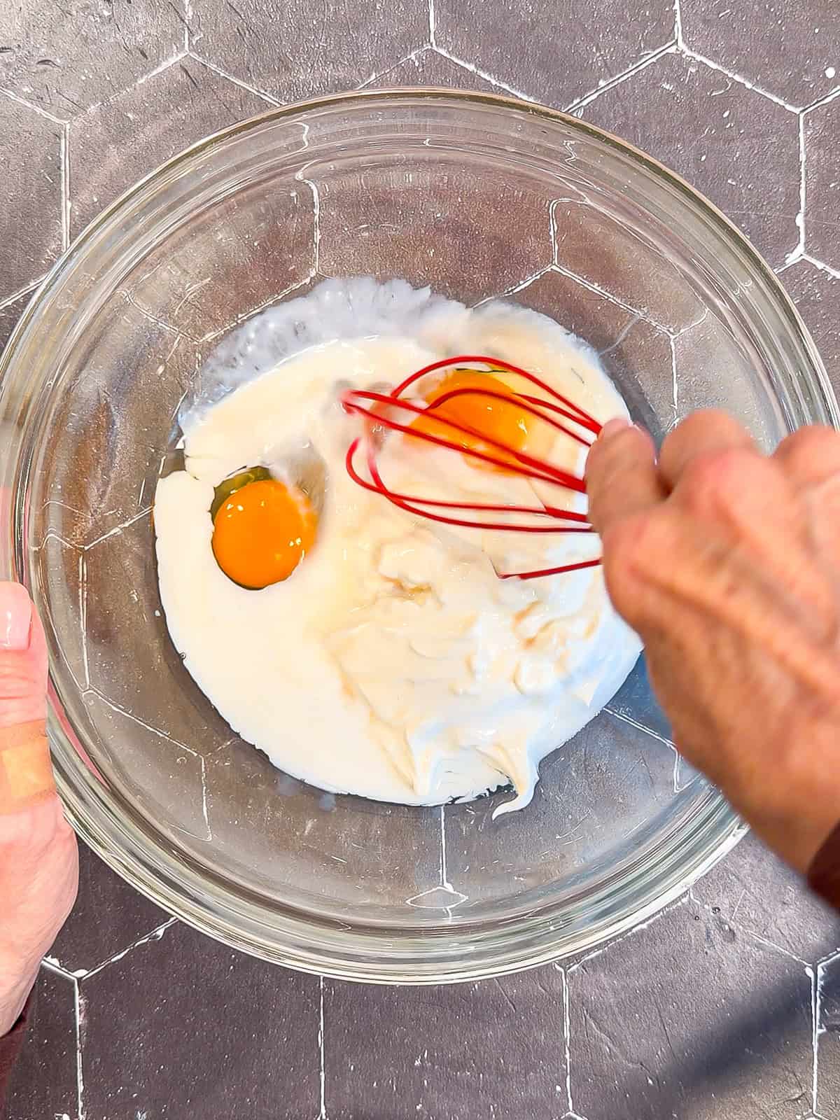 Whisking wet ingredients with a red whisk in a glass bowl.