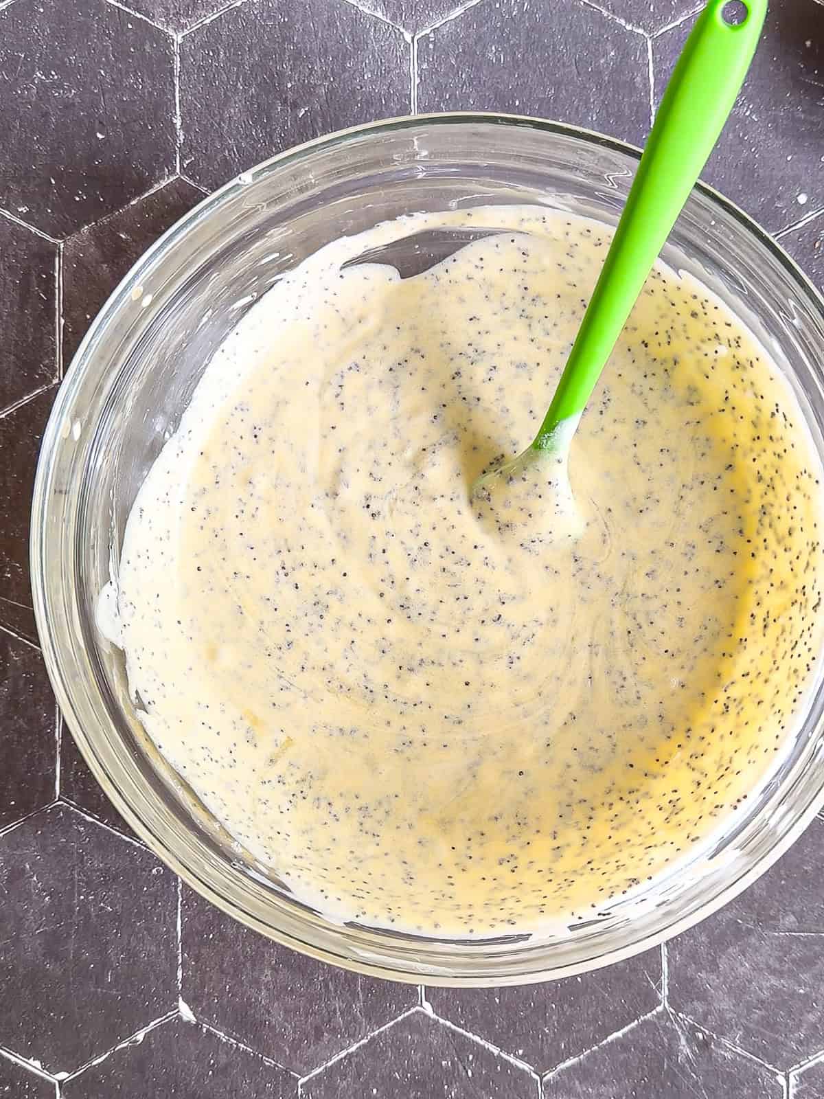 Wet ingredients to make almond poppy seed muffins in a glass bowl with a green spatula.