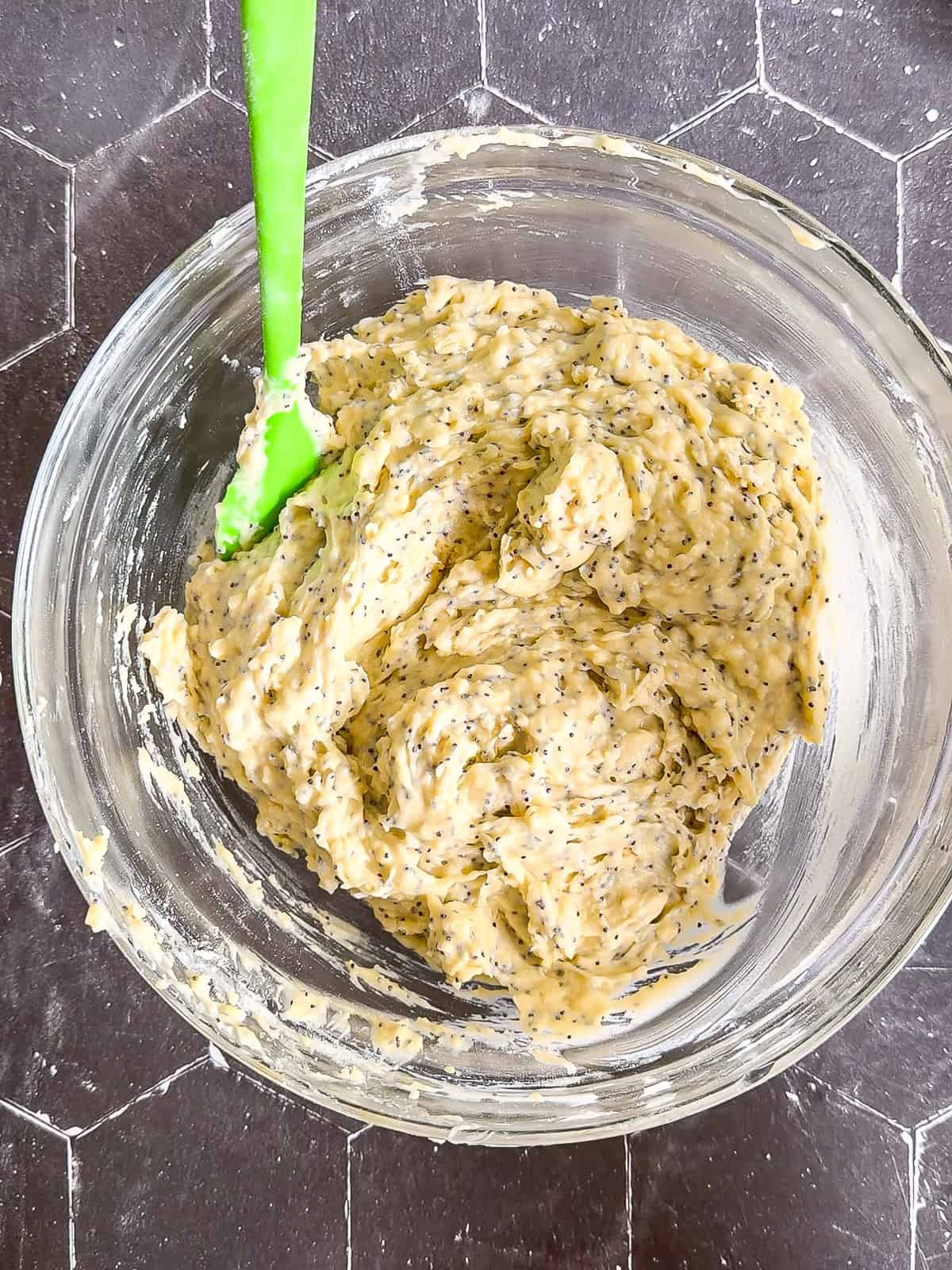 Muffin batter in a glass bowl with a green spatula.