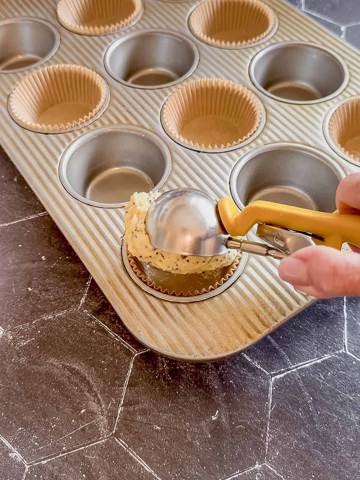 Scooping muffin batter into a lined muffin pan.