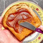 Spread spreading apple butter on a piece of wheat toast.