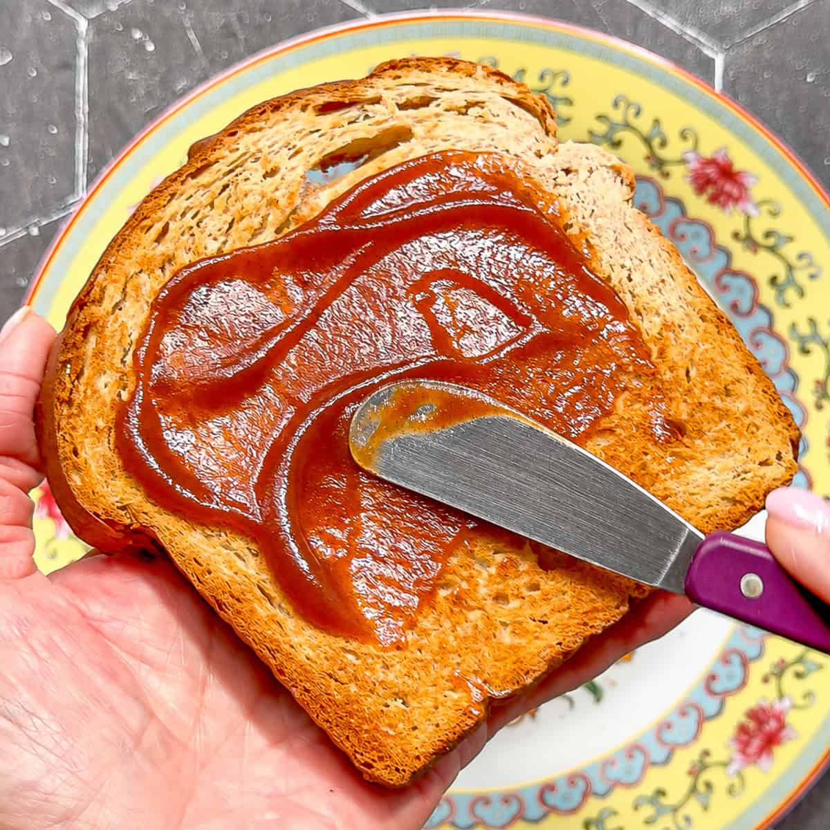 Spread spreading apple butter on a piece of wheat toast.