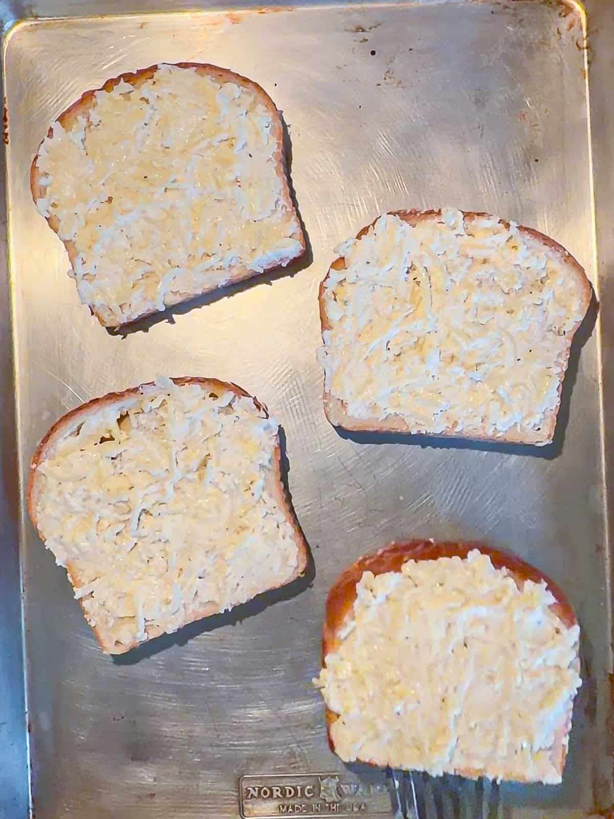 Cheese toast on a hot sheet pan, ready to go in the oven.