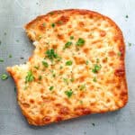 A piece of cheese toast with a bite taken out of it on a sheet pan.