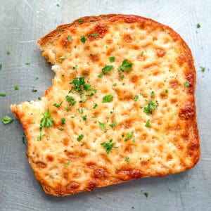 A piece of cheese toast with a bite taken out of it on a sheet pan.