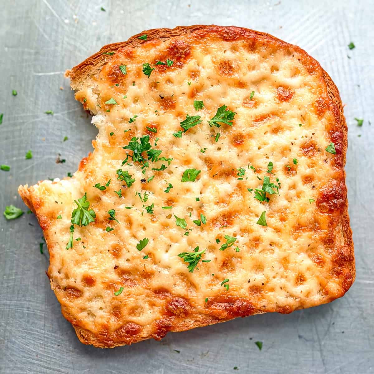 A piece of cheese toast with a bite taken out of it on a sheet pan.