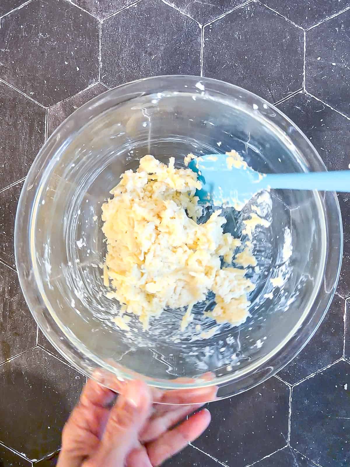 Cheese and mayonnaise mixture in a glass bowl with a blue spatula