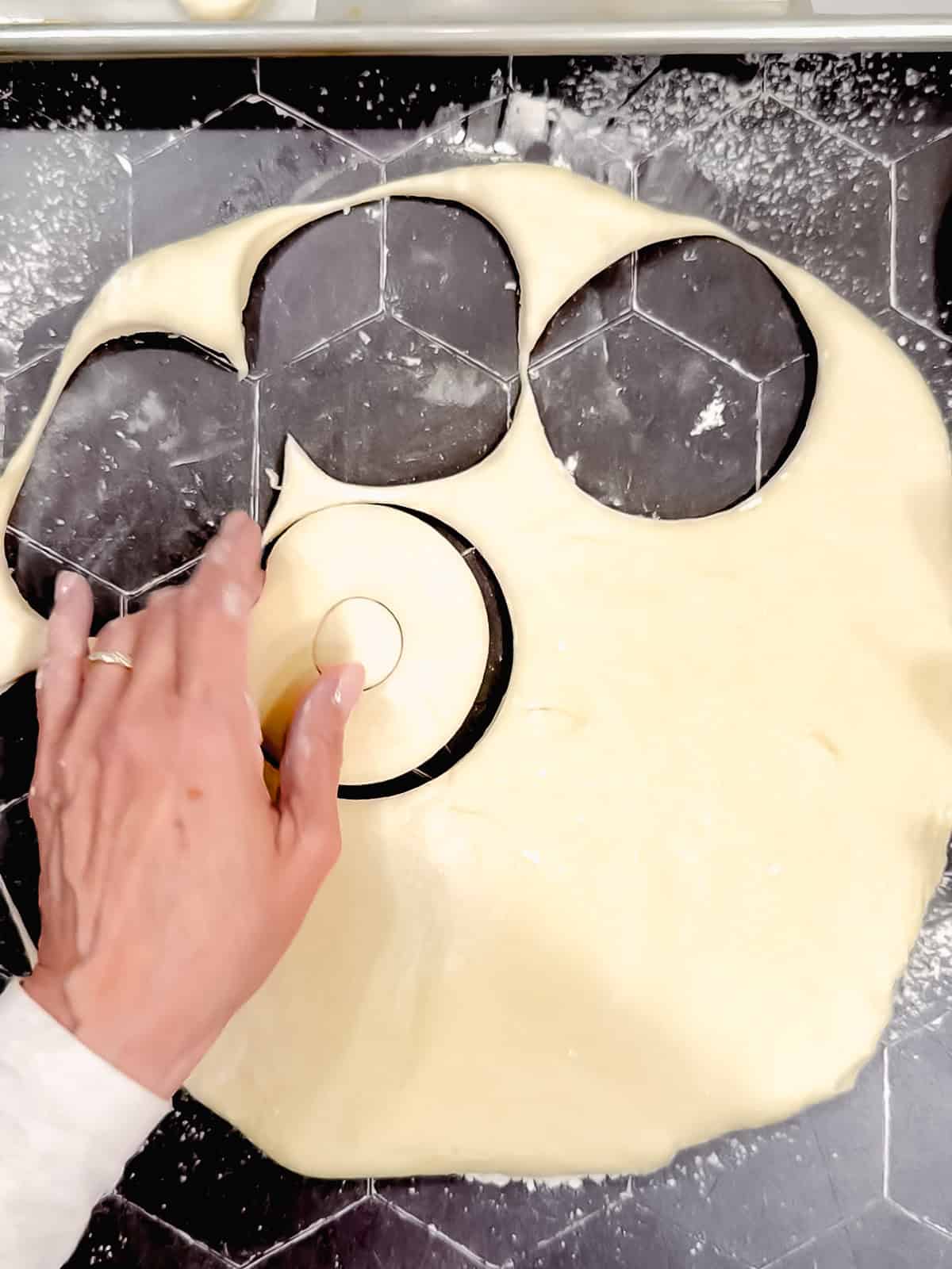 Lifting up a cut out doughnut from a black counter.