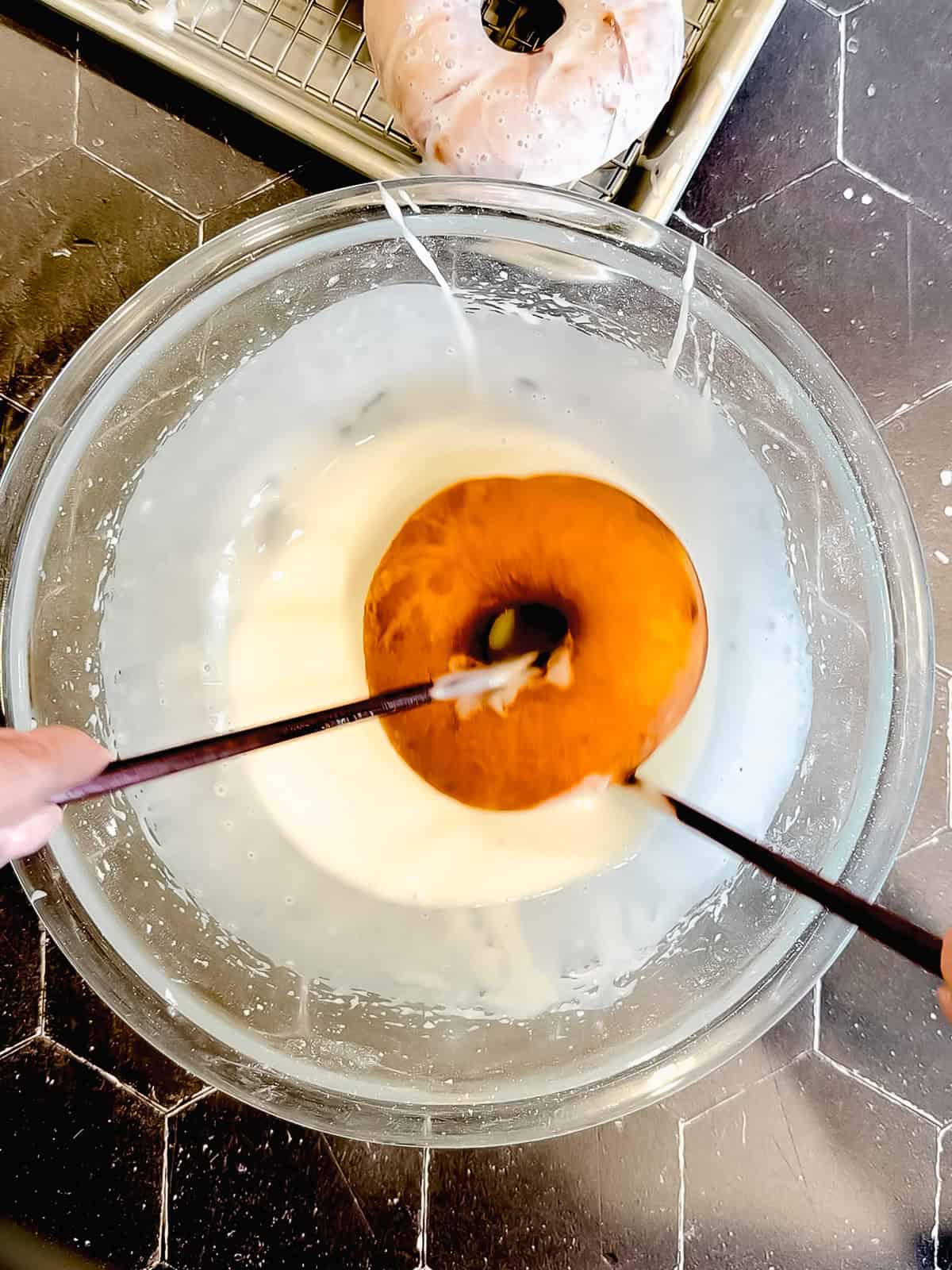 Using two chopsticks to dunk a doughnut into glaze and a glass bowl.