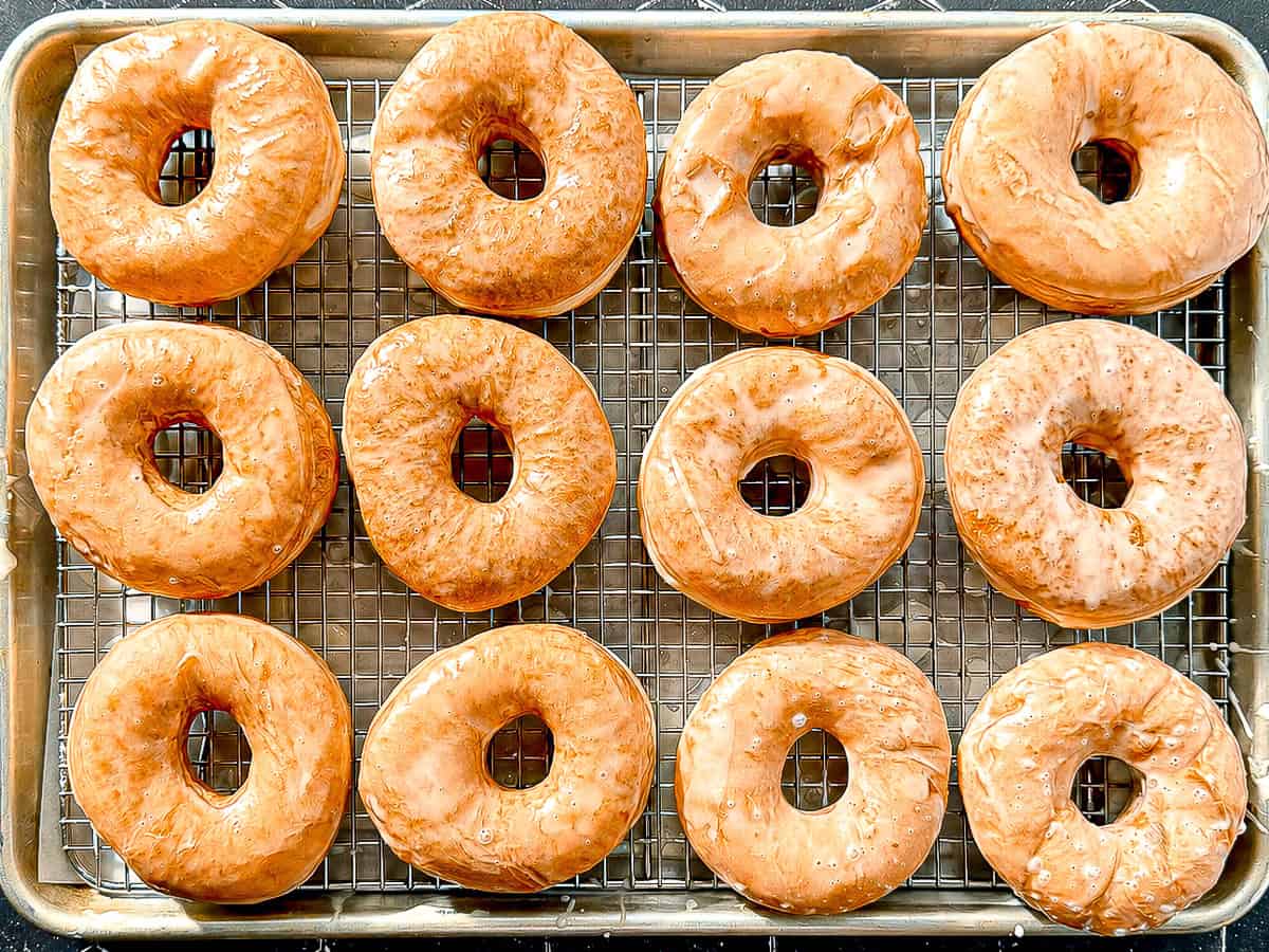 Glazed donuts on a wire rack in a sheet pan.