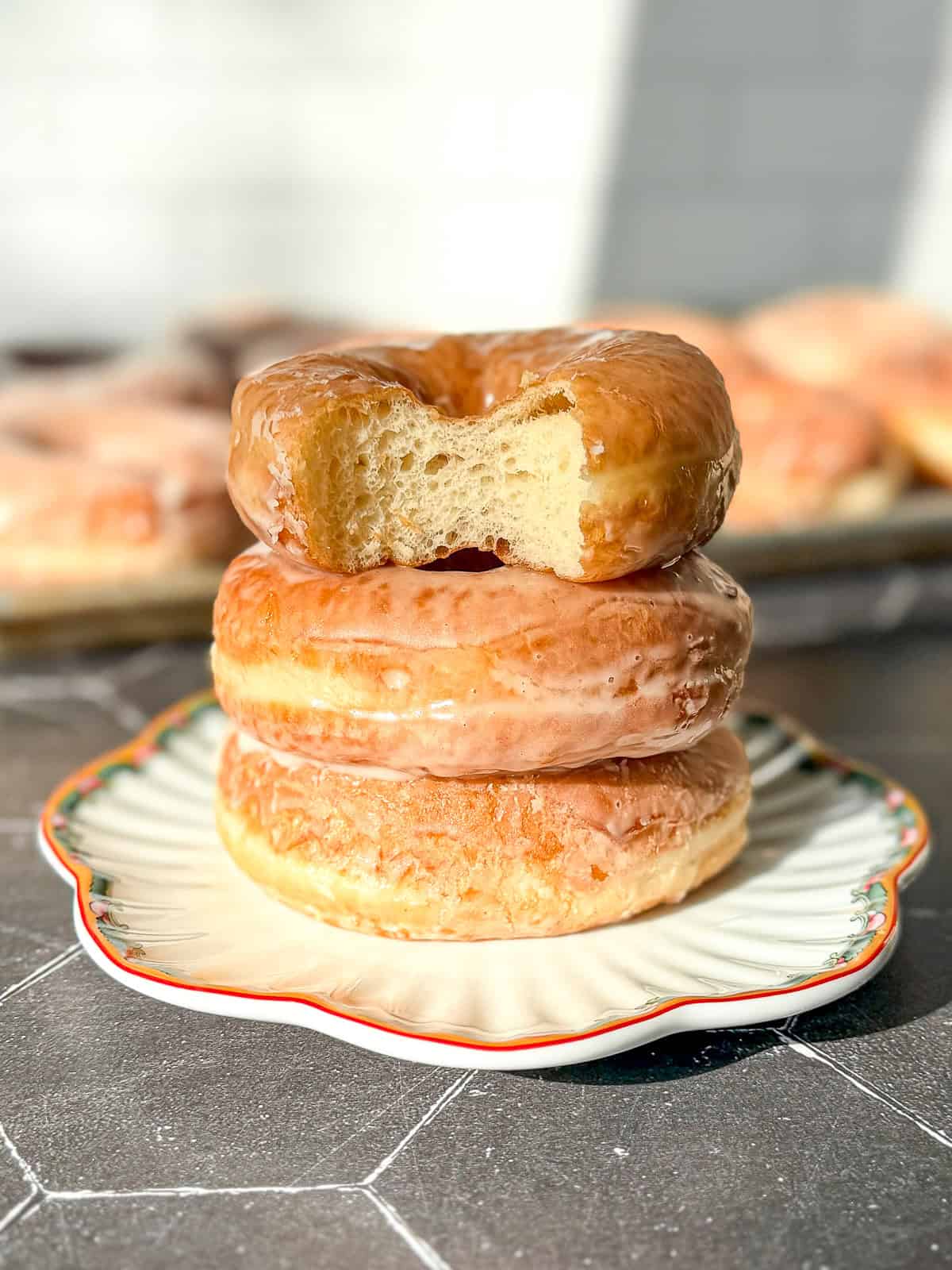 A stack of donuts, the top one with a bite taken out.