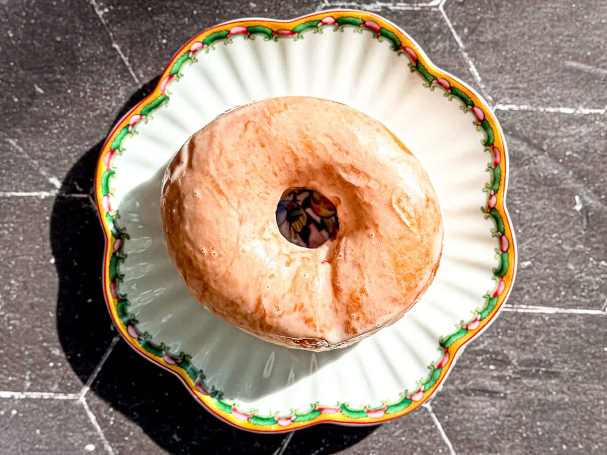 A classic glazed doughnut on a scalloped plate on a black counter.