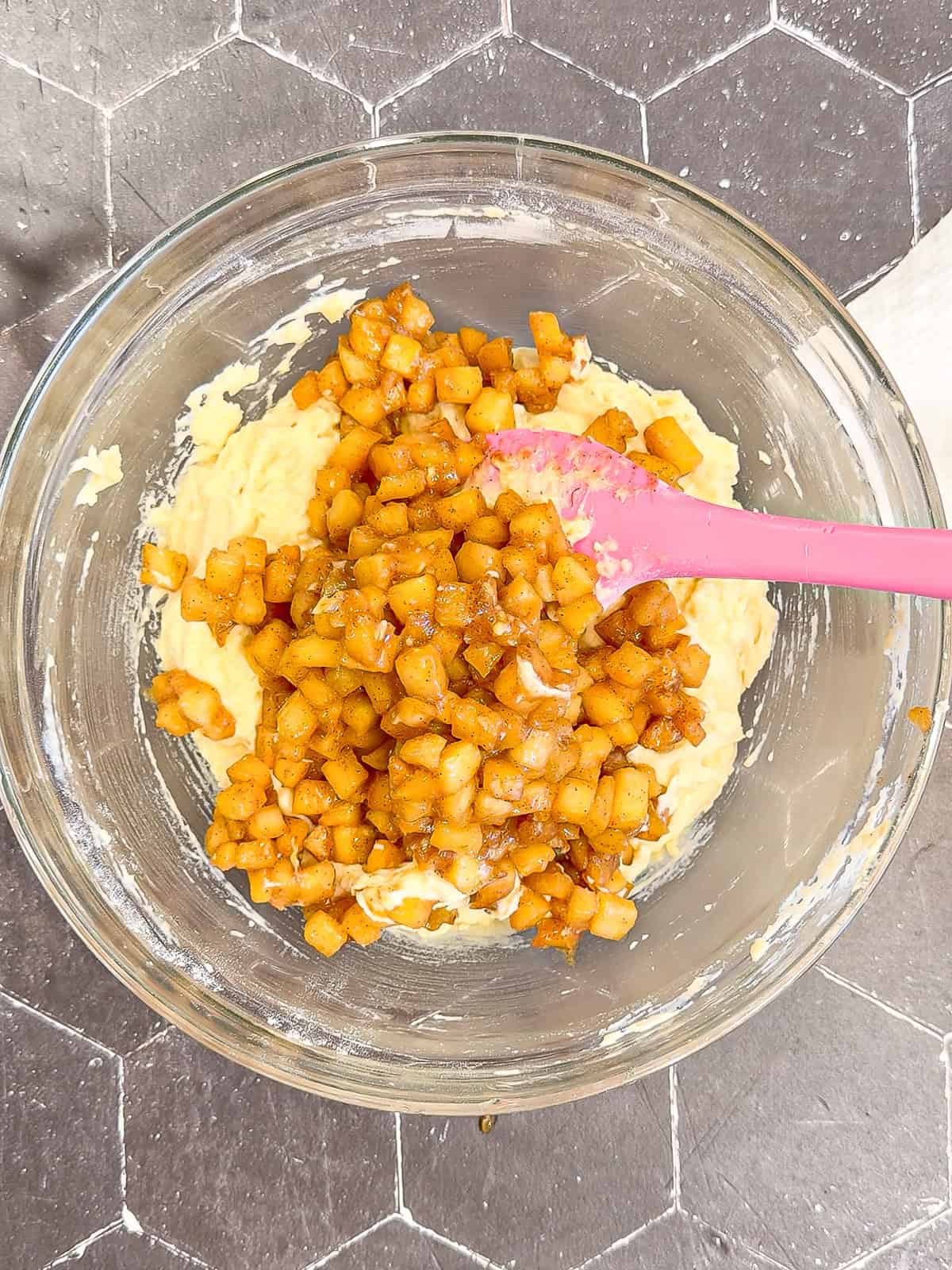 Adding cooled maple apples to fritter batter in a glass bowl.
