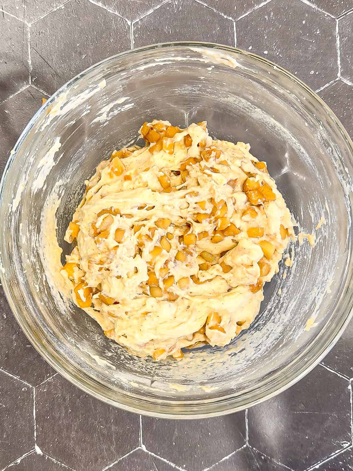 Fritter batter with apples folded in inside of a glass bowl