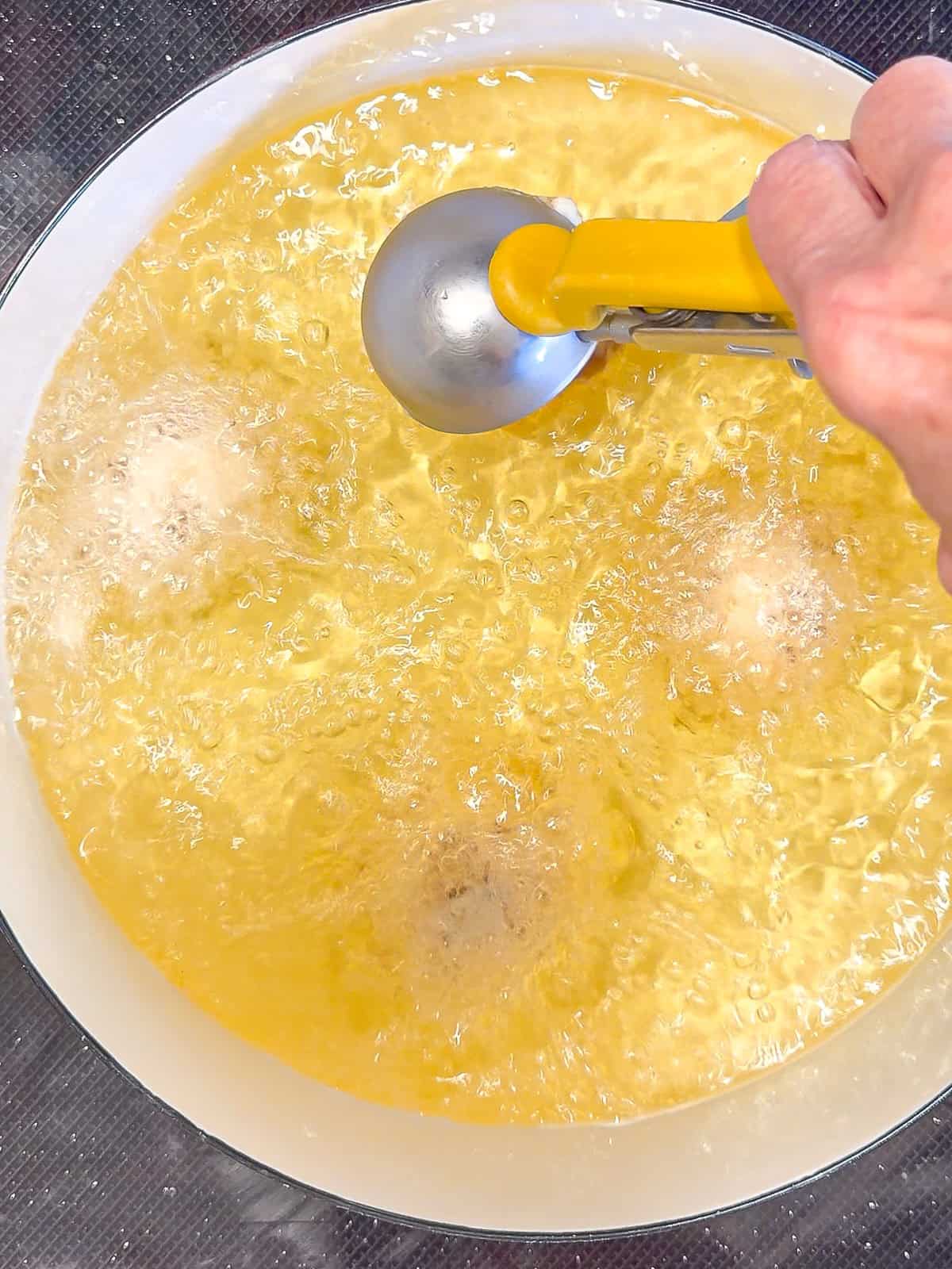 Scooping apple fritter batter into hot oil in a Dutch oven.