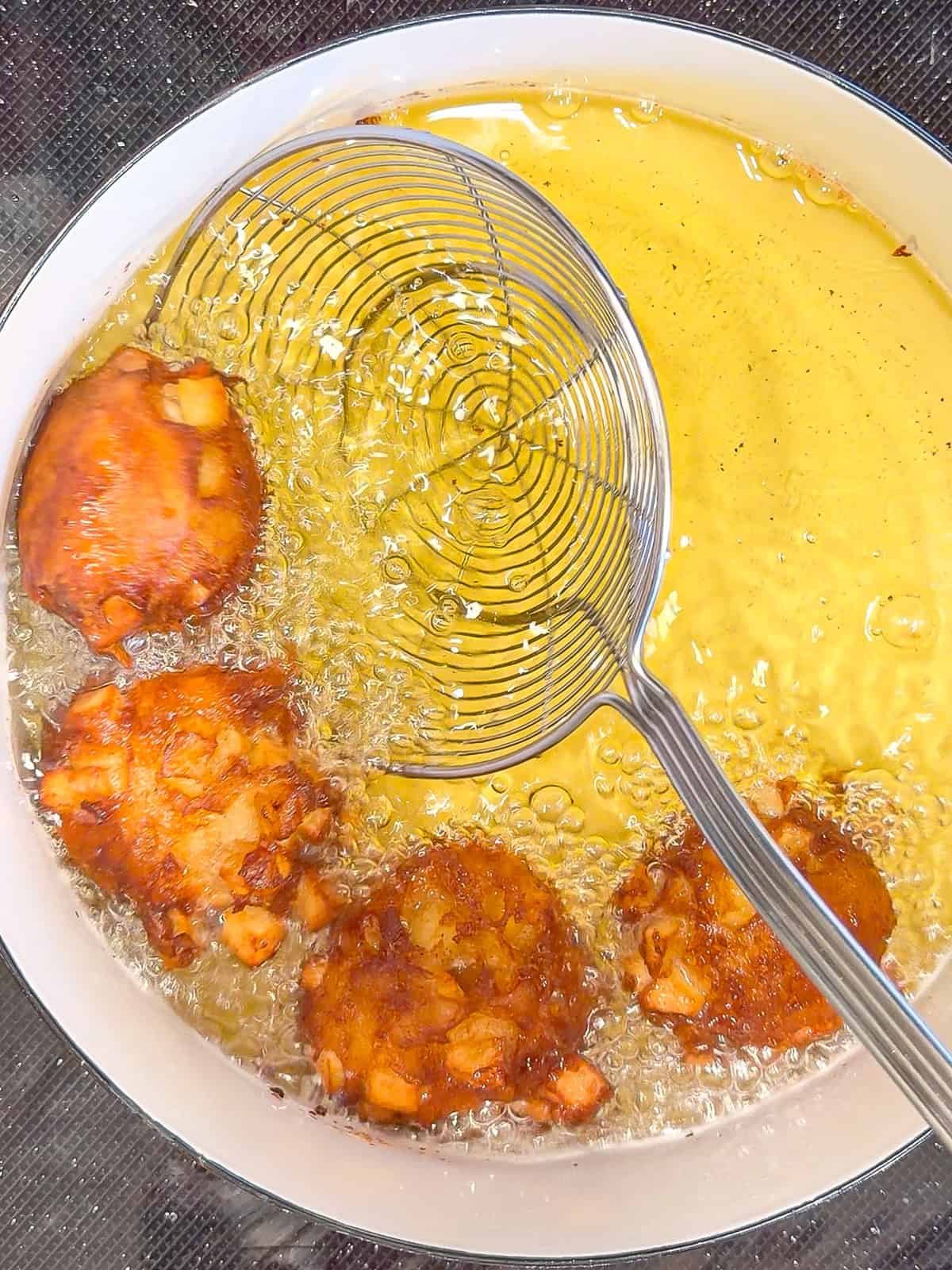 Using a spider strainer to retrieve apple fritters from hot oil.