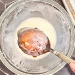 Glazing an apple fritter over a glass bowl.