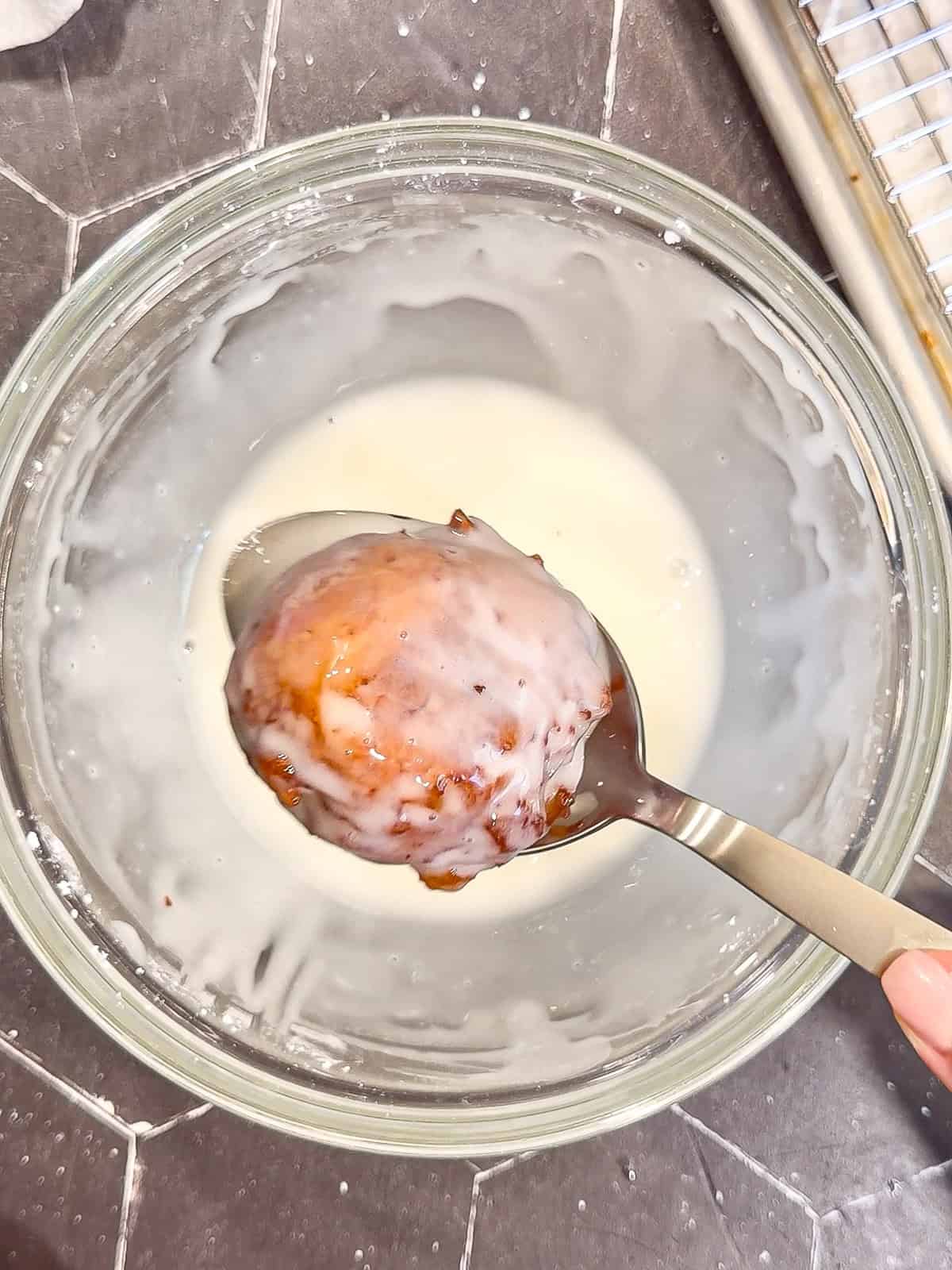 Glazing an apple fritter over a glass bowl.