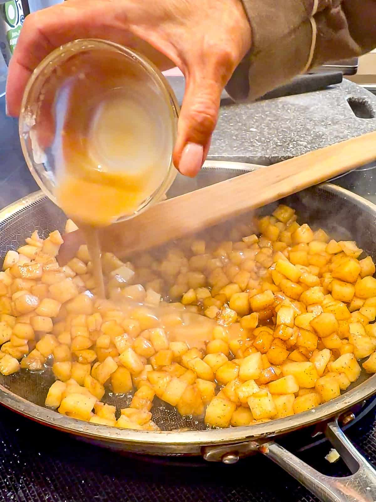 Adding maple syrup mix mixed with cornstarch into cooked apples in a skillet.