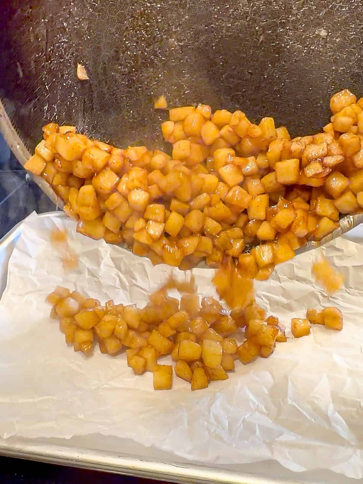 Transferring cooked maple apples onto a parchment paper covered sheet pan to cool.