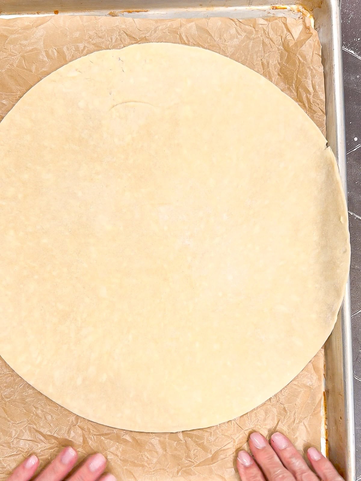 Placing a pie crust on a piece of parchment paper on a sheet pan.