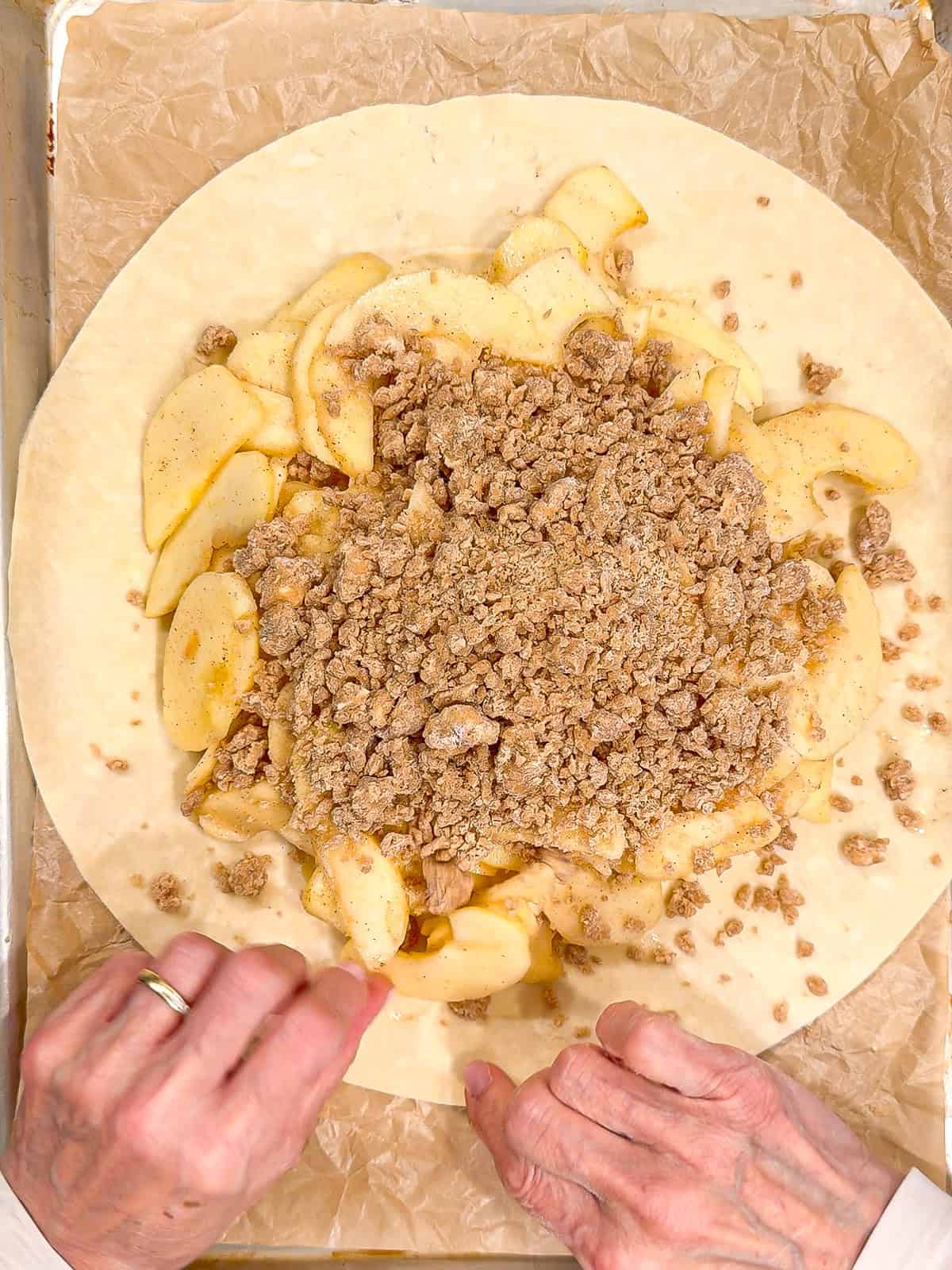 Placing streusel on top of apples on a piecrust.
