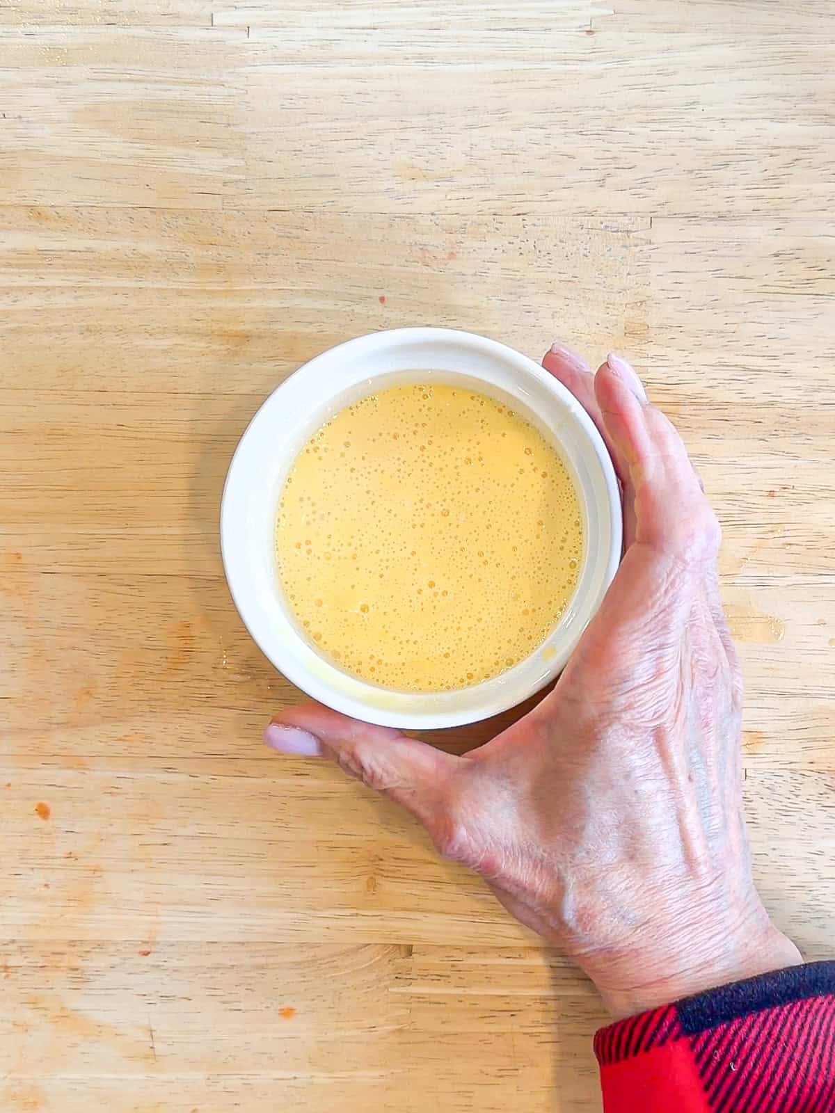 Whisked egg ready to microwave in a white ramekin.