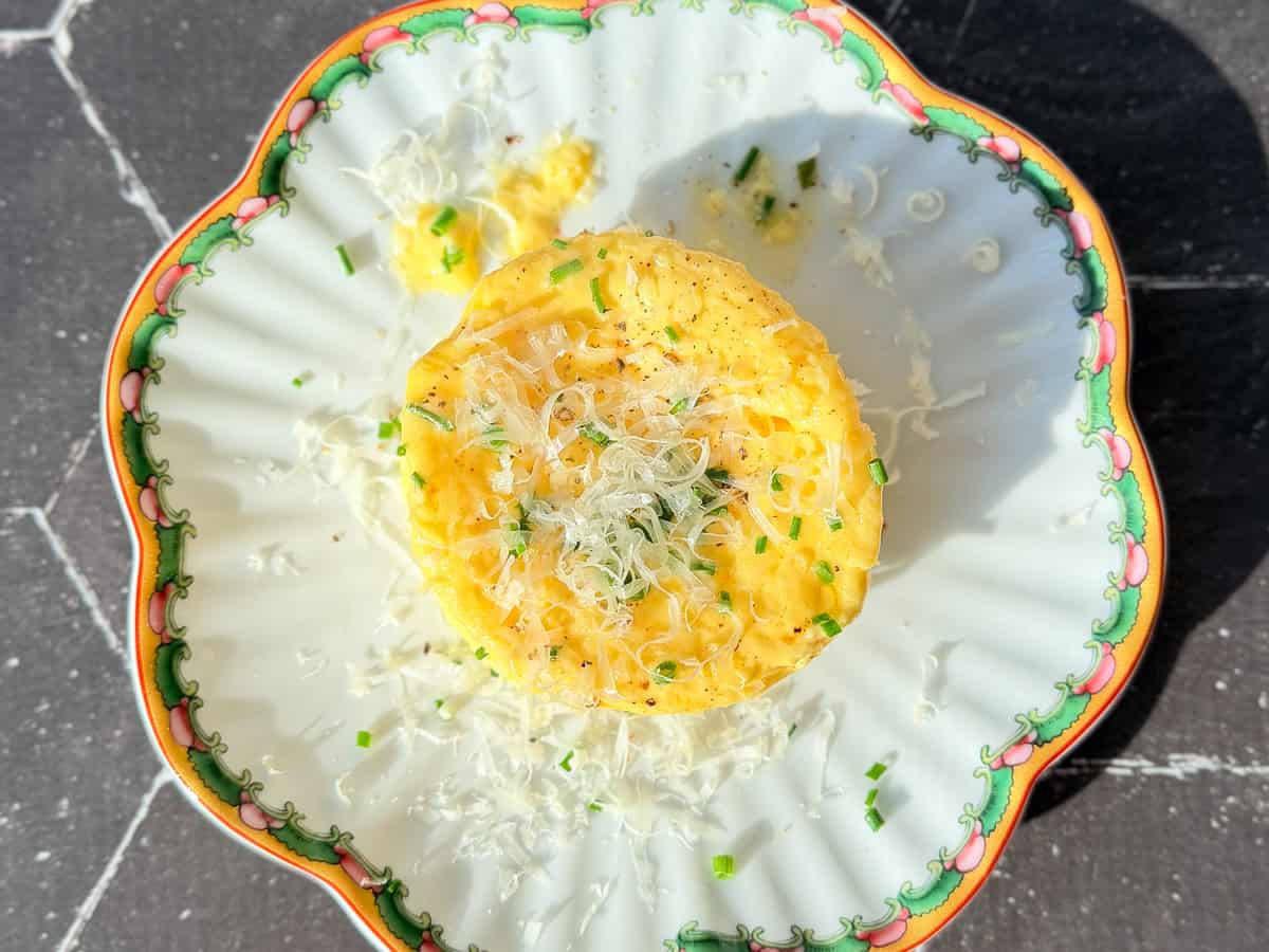A microwave omelette with grated Parmesan, black pepper, and chives on a white scalloped plate.